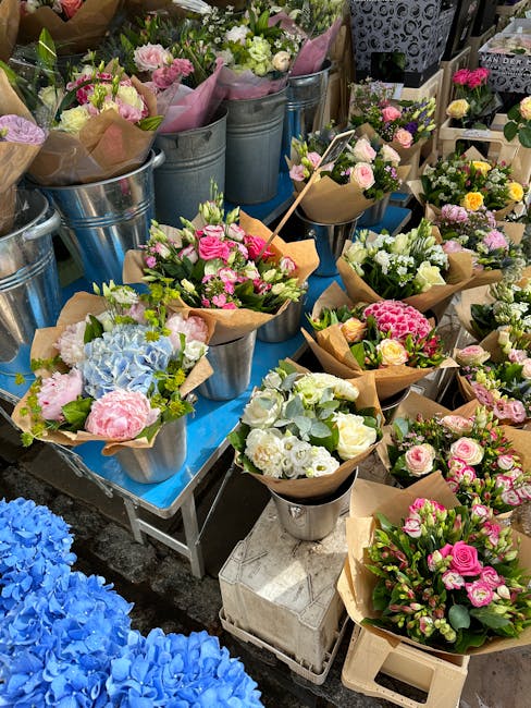 A vibrant display of freshly arranged flower bouquets at a floral shop, featuring various pastel and bright colors including pink, white, blue, and yellow. The bouquets are wrapped in kraft paper and 