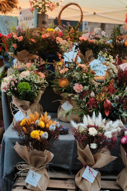 A vibrant display of freshly arranged flower bouquets at an outdoor market stall, featuring a variety of blooms including pink roses, white daisies, yellow chrysanthemums, and deep red anthuriums. The