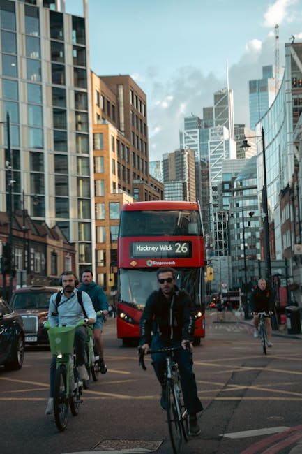 This image depicts an urban street scene in Hackney with three cyclists at the foreground, including a man wearing sunglasses and a dark jacket, riding alongside other cyclists. Behind them, a double-